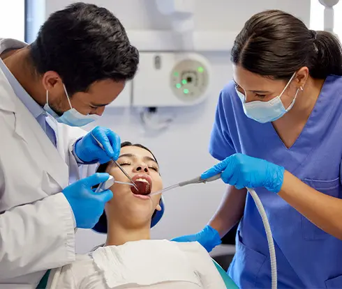 A dental assistant and dentist inspect the mouth of a patient