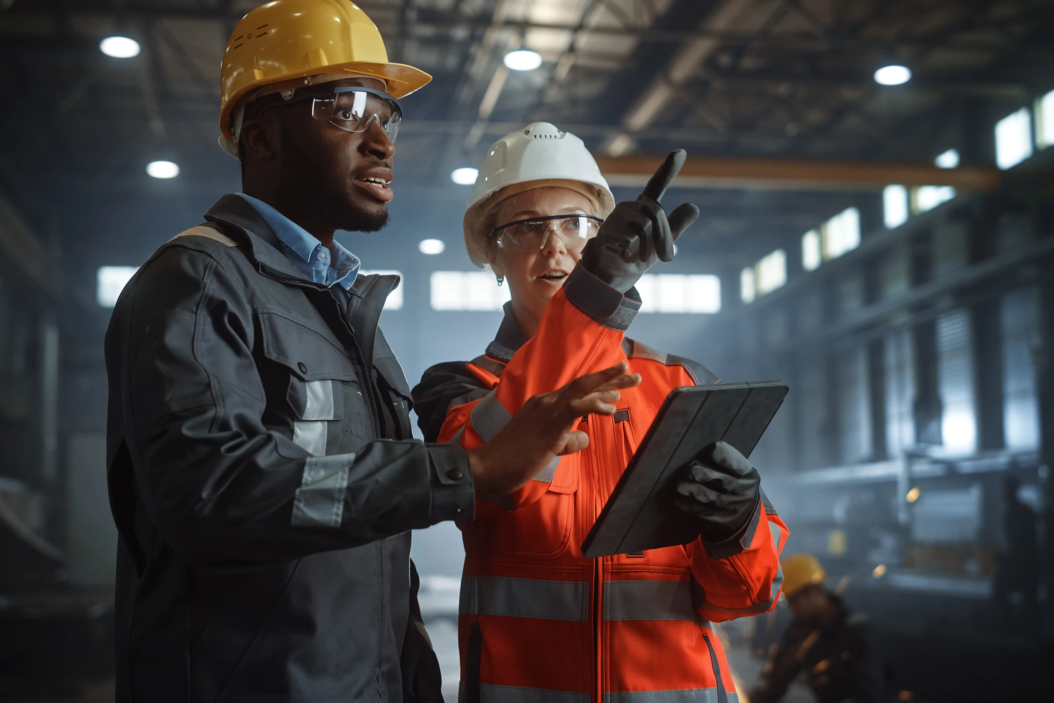 Two men wearing safety equipment look down on machining equipment